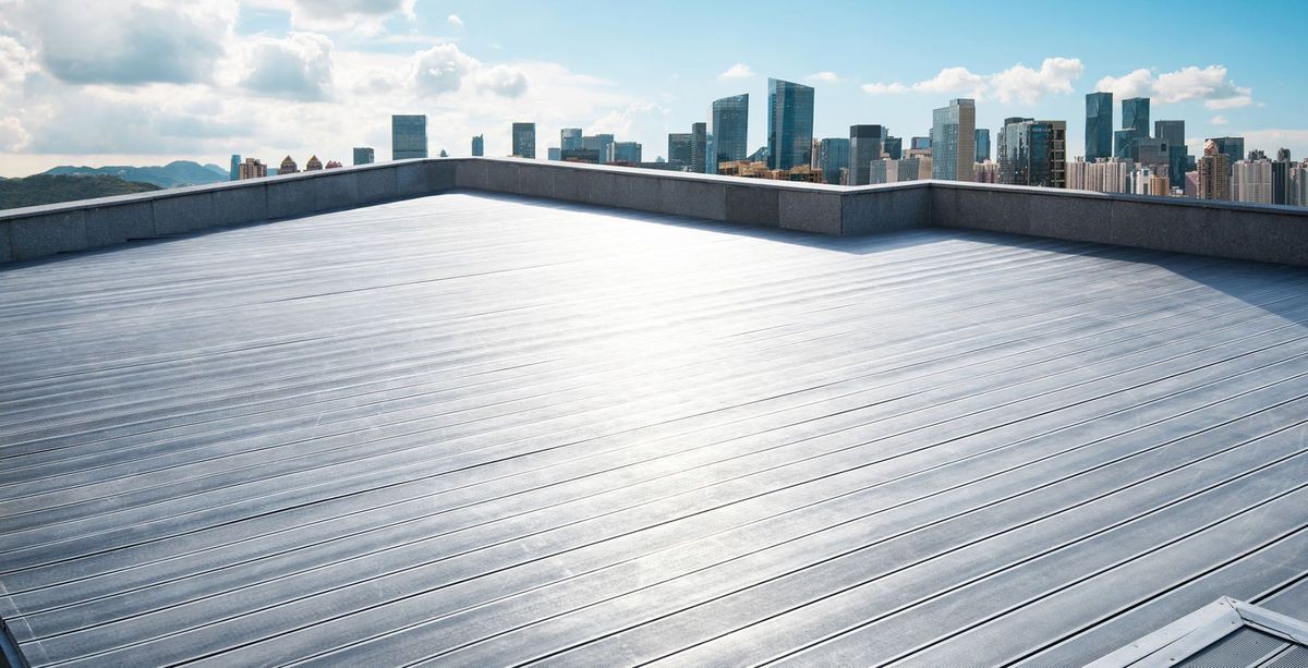 A wide-angle view of a flat, light-gray industrial rooftop overlooking a distant city skyline under a sunny sky.