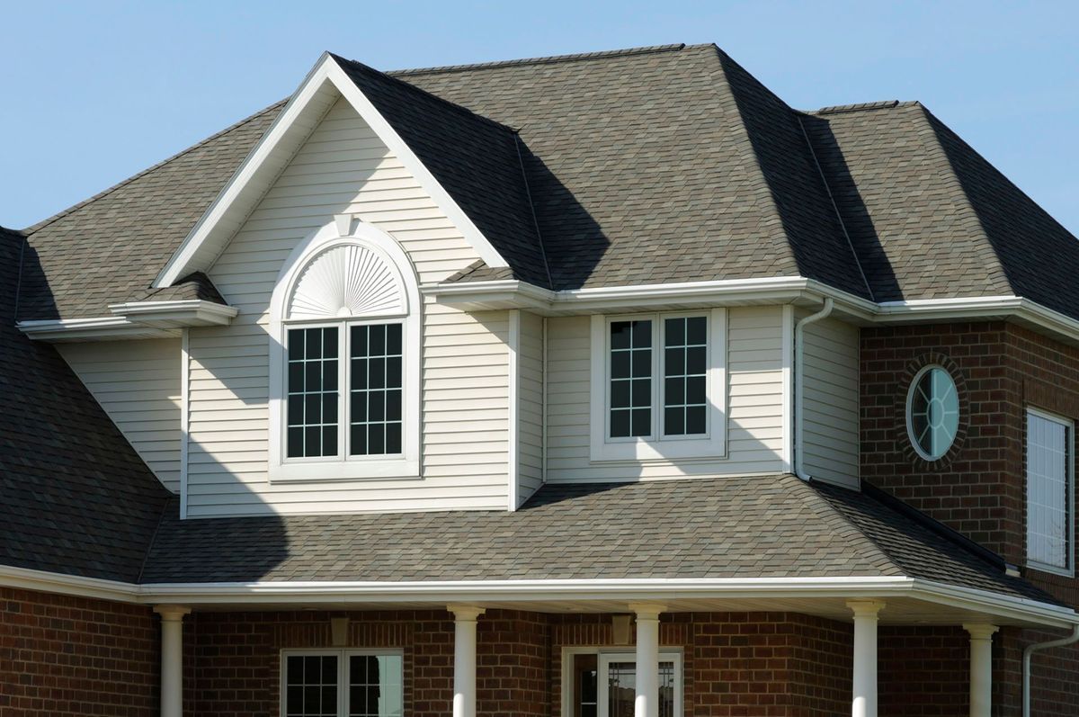 A residential house featuring brick lower walls, cream siding on upper levels, an arched window, and gray roof shingles.