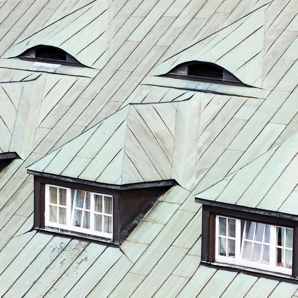 Light green metal roof with two rectangular dormer windows and two small, arched eyebrow windows above them.