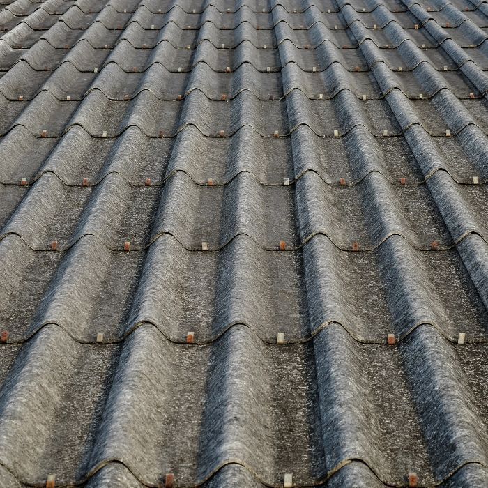 A high-angle view of a grey, weathered corrugated roof with repeating rows of wave-shaped tiles.