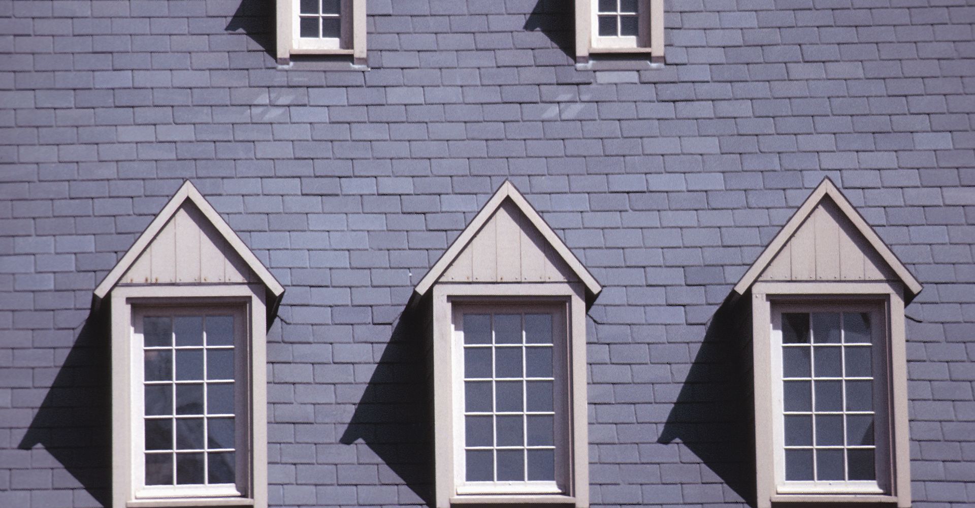 A slate-gray shingled wall with three peaked dormer windows on the bottom and two small windows at the top.