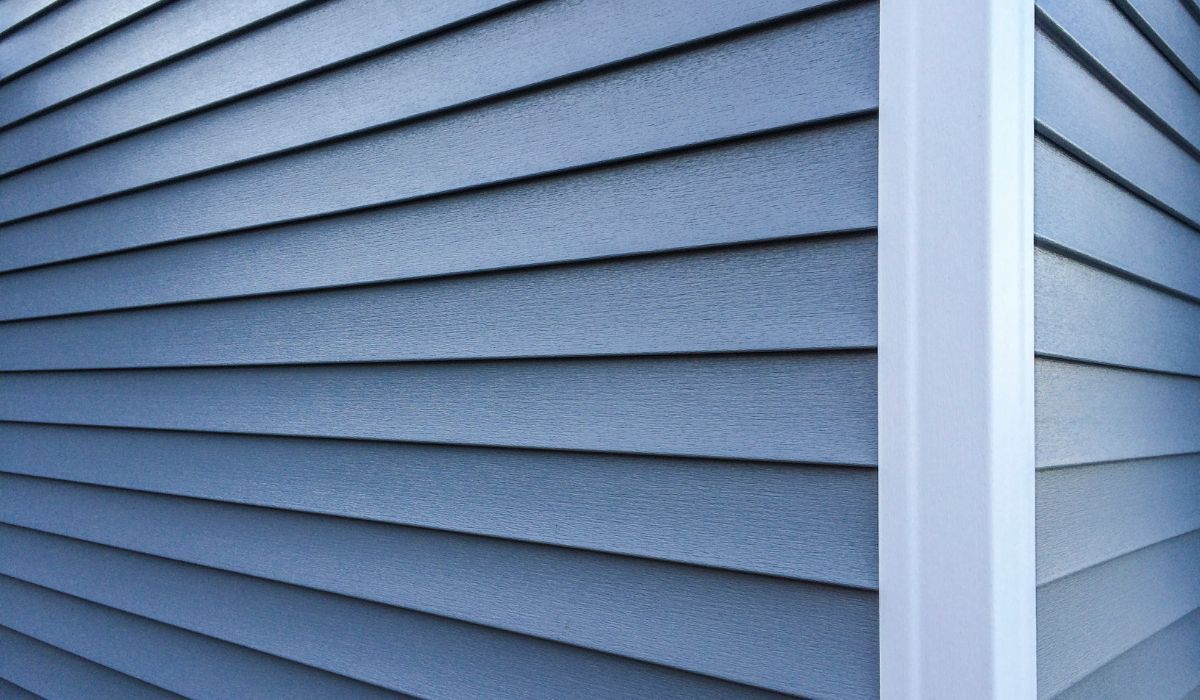 A close-up view of a blue, horizontal lap-style siding on a house, featuring a white corner post.