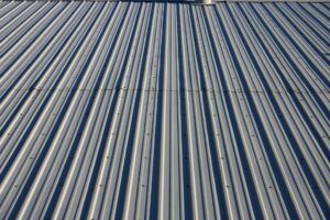 A close-up, angled view of a gray corrugated metal roof with repeating vertical ridges and visible fasteners.