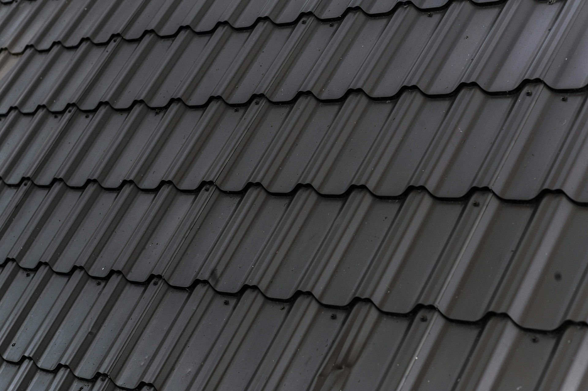 A close-up view of a roof covered in uniform, dark gray metal shingles with a repeating, ridged pattern.