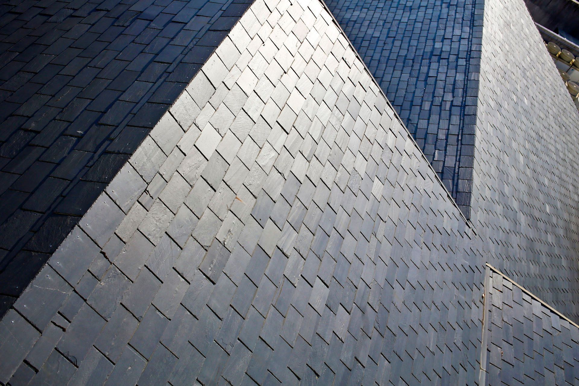 A high-angle view of multiple steeply pitched roof planes covered in dark, rectangular slate shingles.