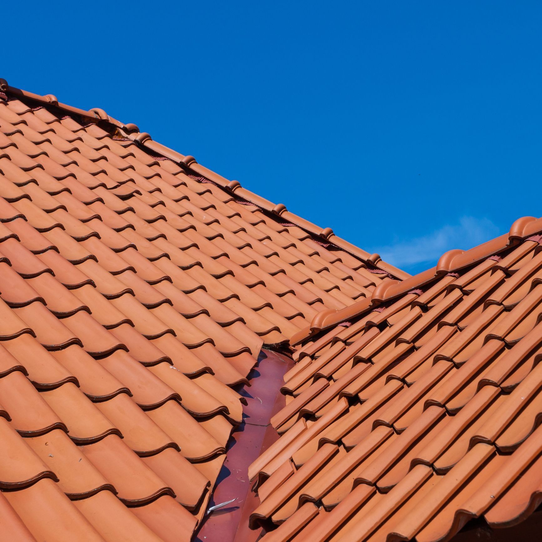 Red-orange clay roof tiles arranged in a peaked pattern against a clear blue sky.
