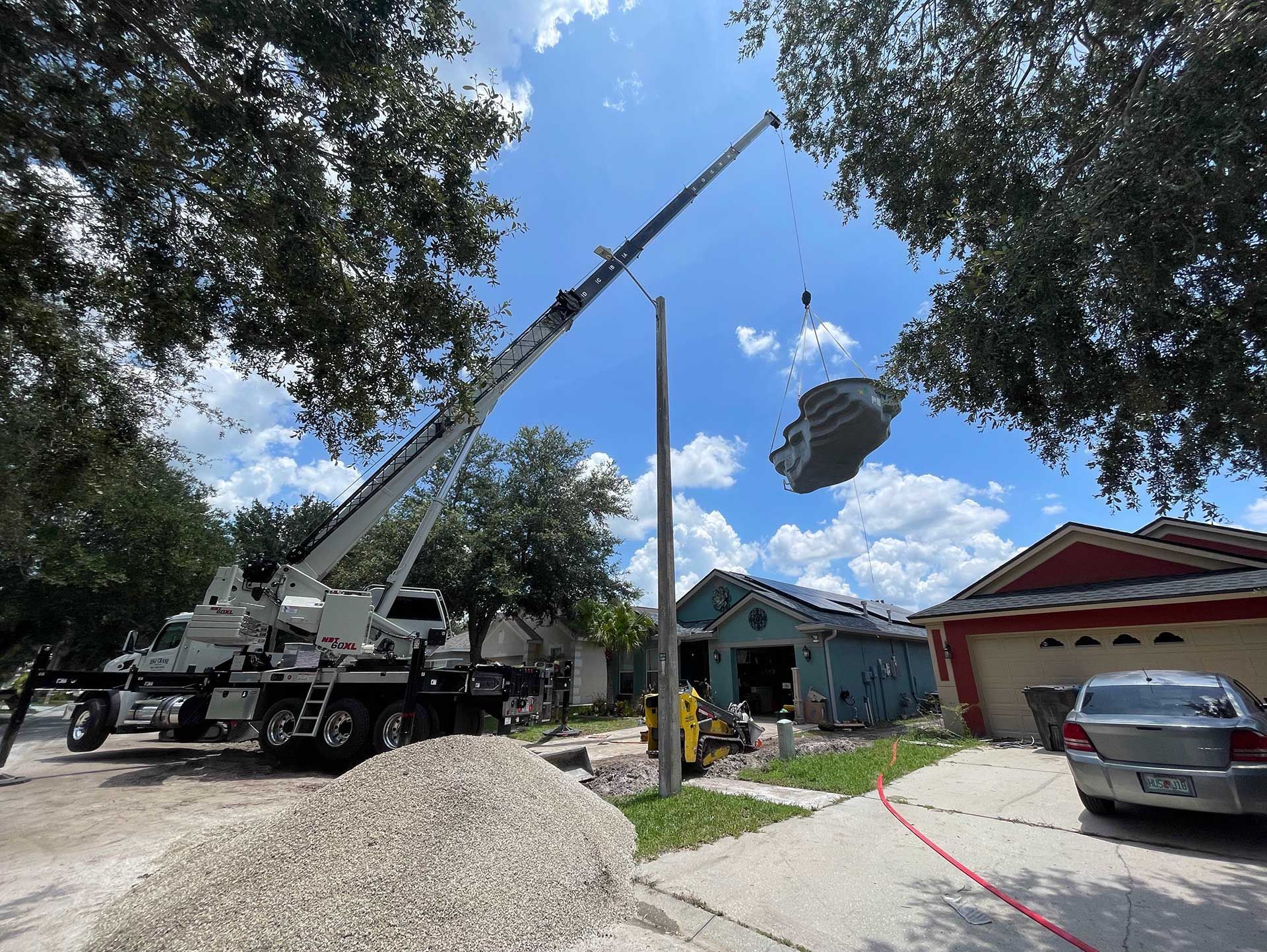 A crane is lifting a swimming pool over a house