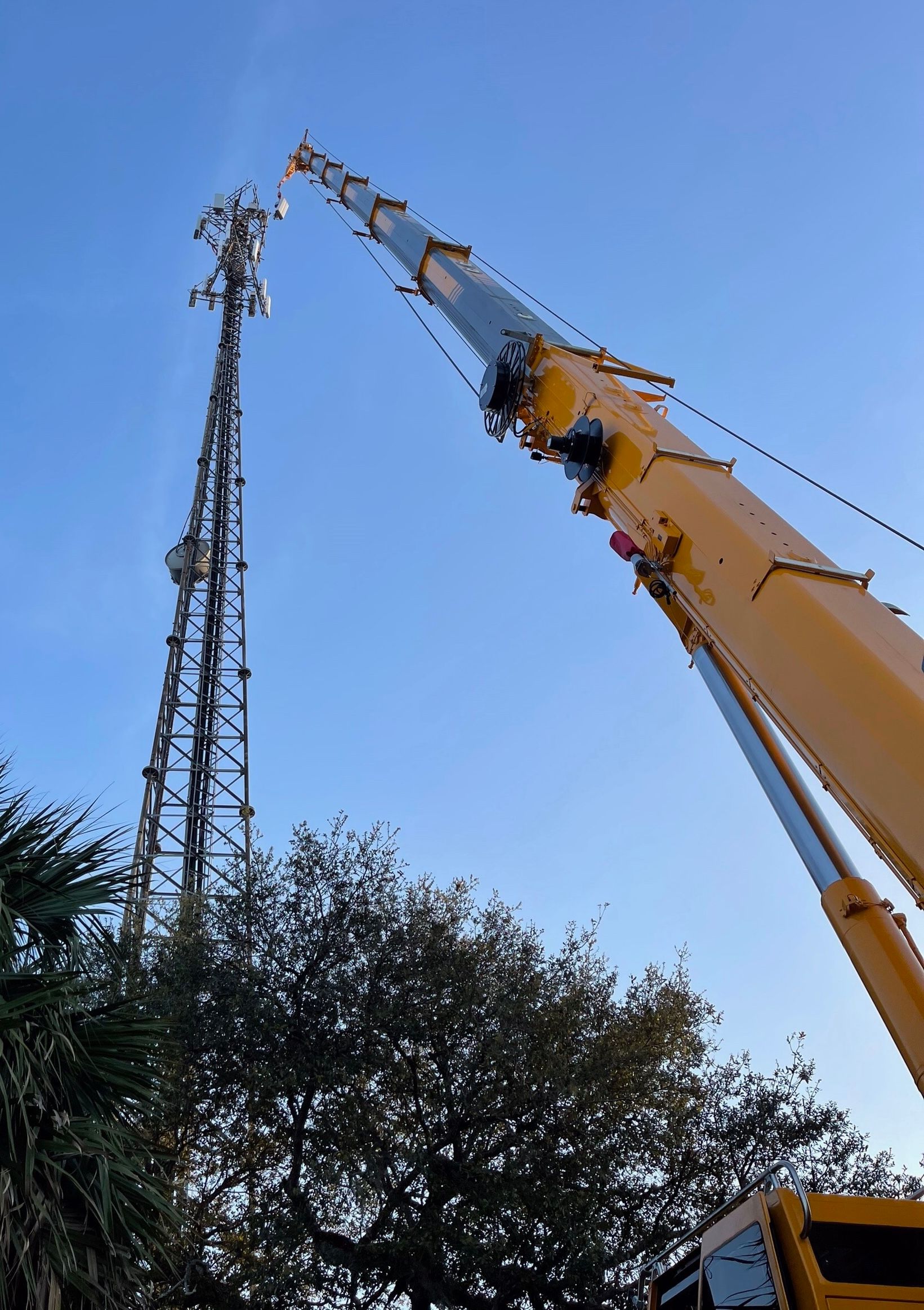 A large yellow crane is working on a telephone tower