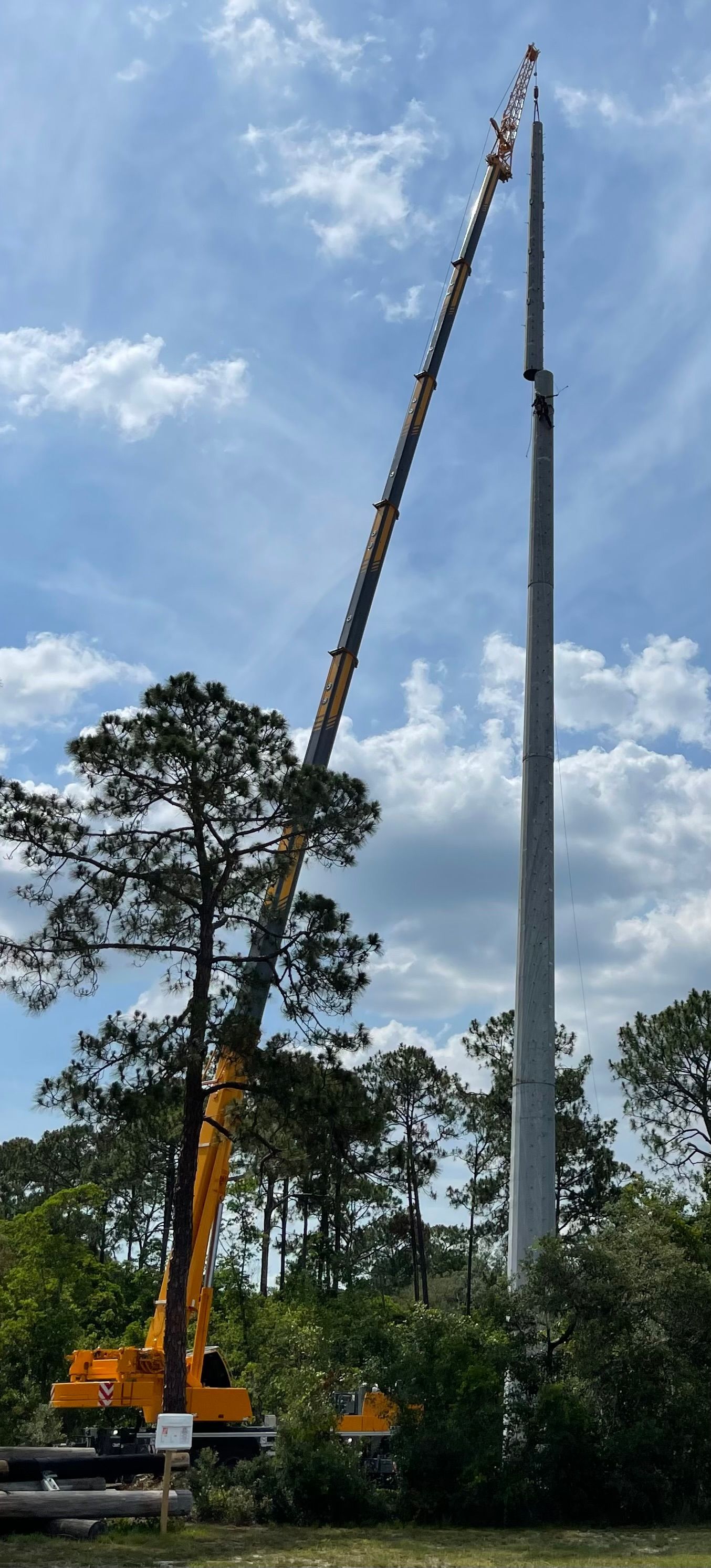 A crane is lifting a pole in a field with trees in the background.
