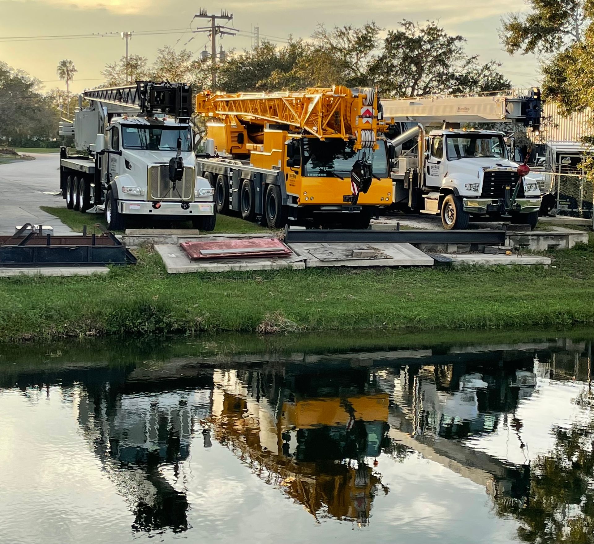 Several construction trucks are parked next to a body of water