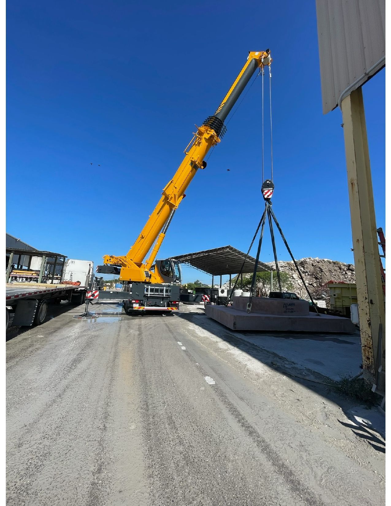 Yellow crane lifting a gray load at a construction site under a clear blue sky