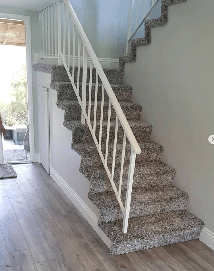 A staircase with gray patterned carpet and a white handrail, leading up against a light gray wall in a home interior.