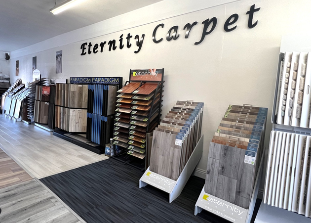 The showroom interior of Eternity Carpet displays various flooring samples, including wood planks and textured materials.