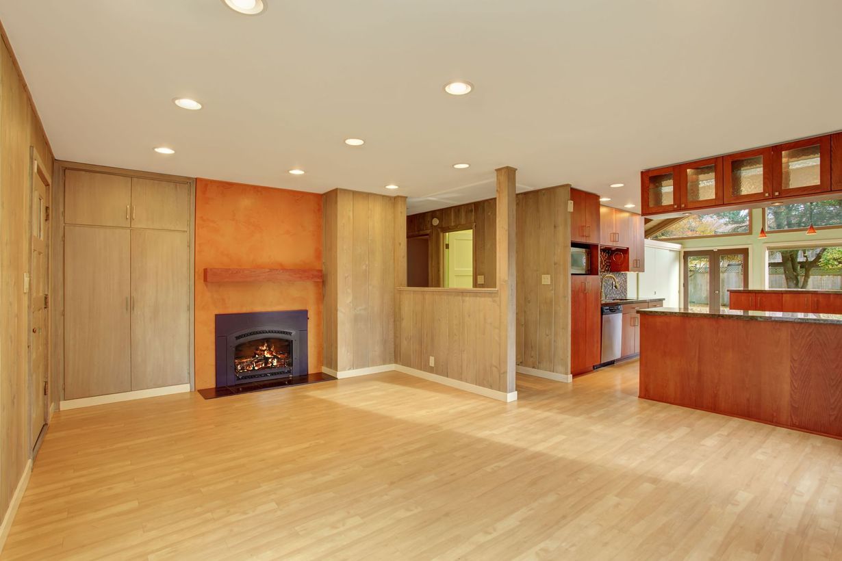 An open-plan living room with light wood floors, a fireplace set in an orange wall, and a wooden kitchen island counter.