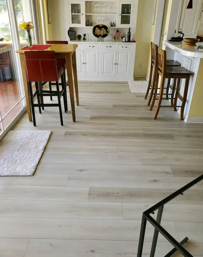 A bright dining area features light wood-look flooring, a small wooden table with red chairs, and a white buffet cabinet.
