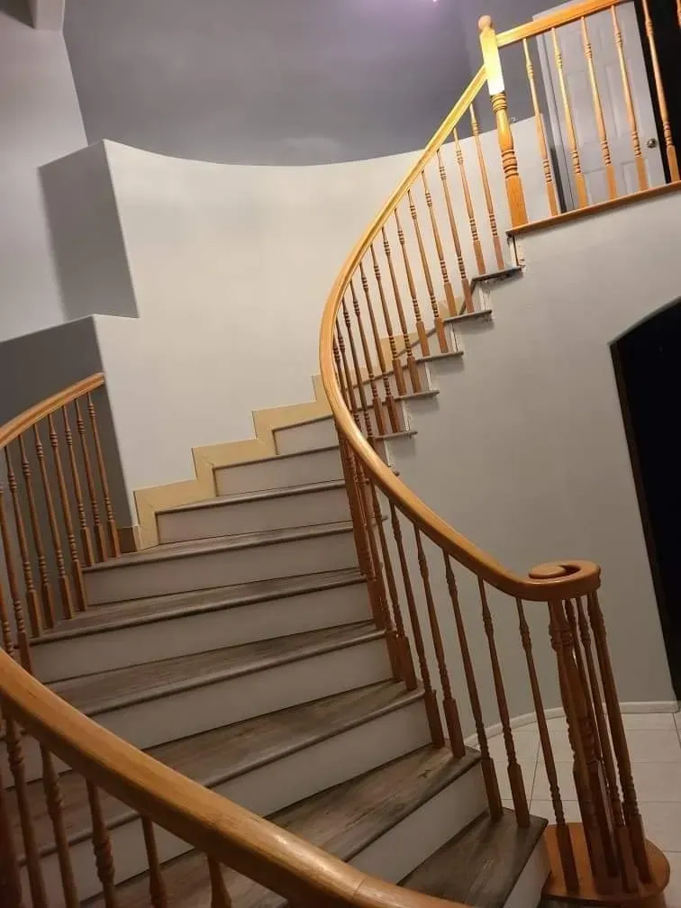 A curved staircase with wooden railings and steps ascending to a landing in a neutrally colored hallway.