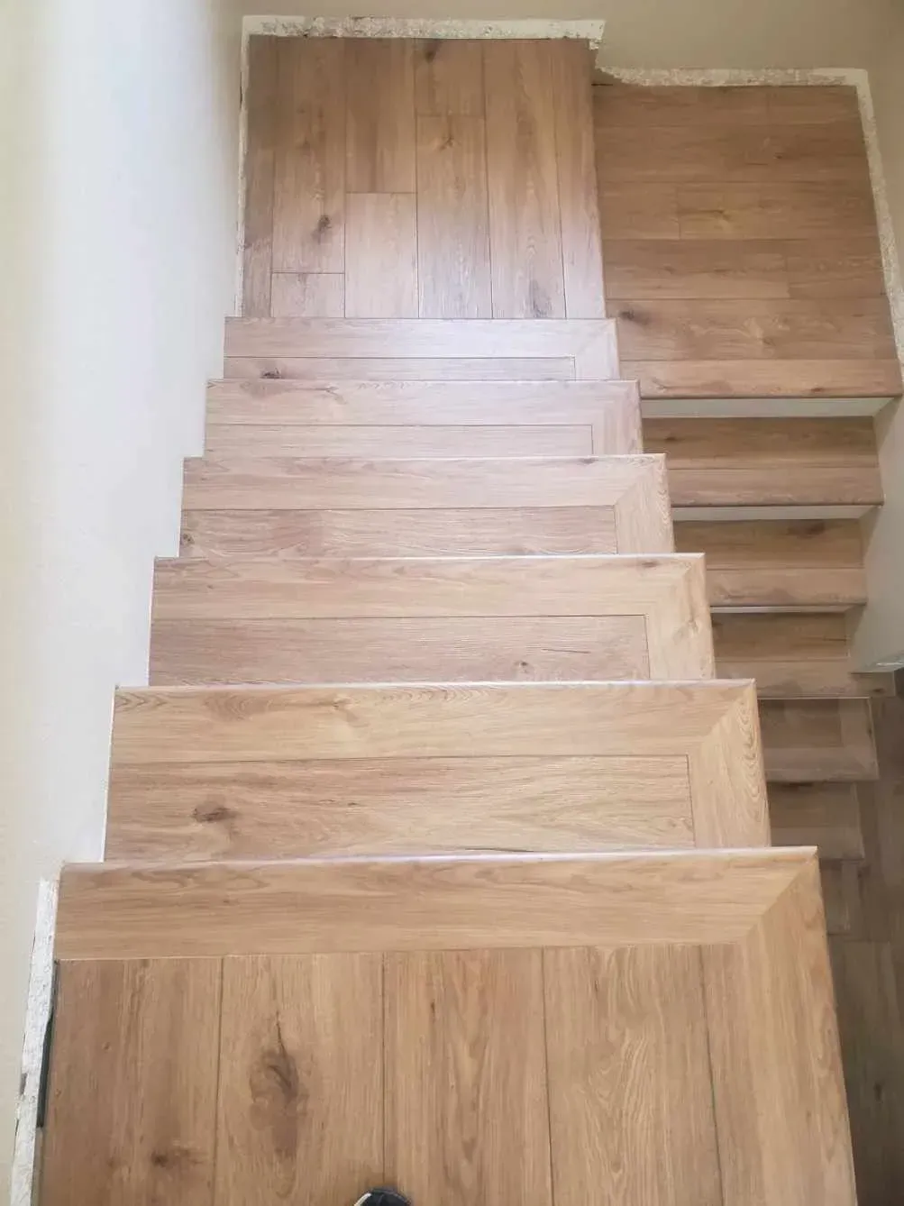 Top-down view of wooden stairs and a landing featuring light-toned, wood-grain planks.
