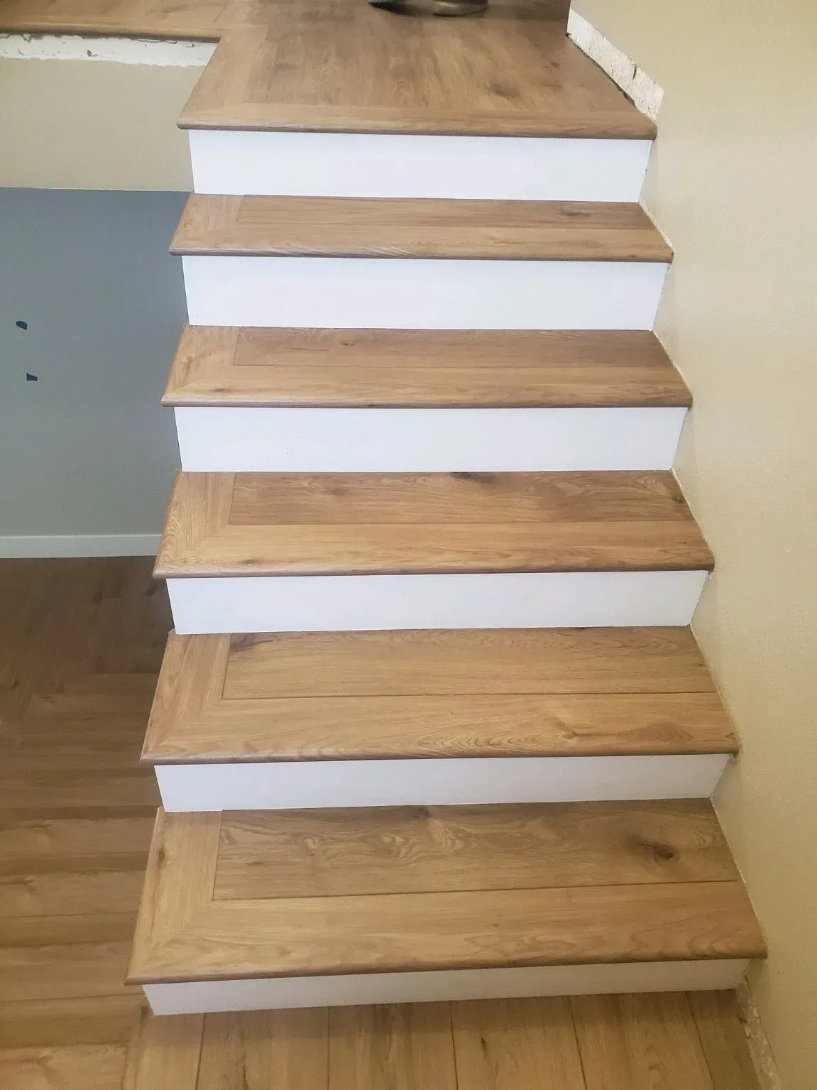 A staircase featuring light wood-toned treads and white risers, viewed from the bottom looking upward.