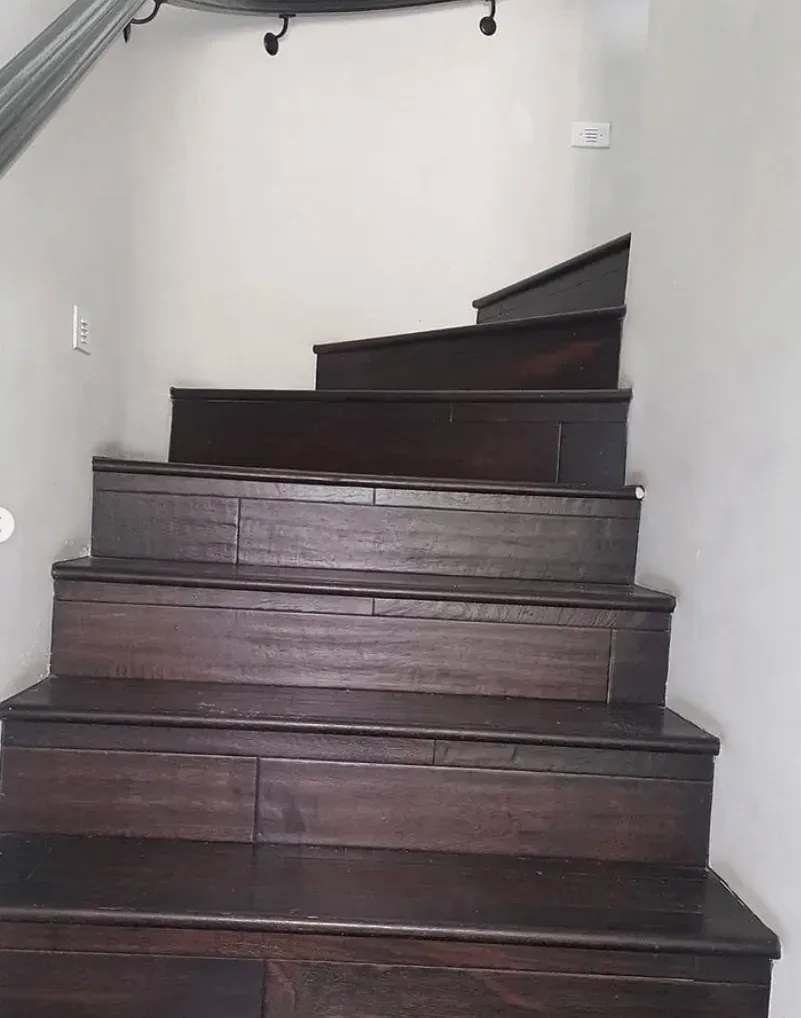 A dark wooden staircase leads upward in a plain white hallway, with a curved handrail visible on the left.
