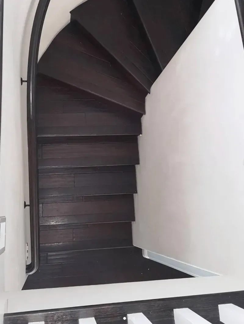 A curved staircase with dark wooden treads ascends between white walls.