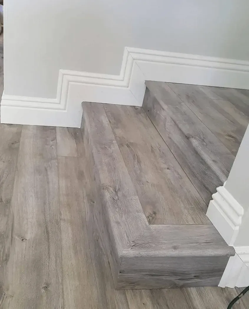A staircase featuring light-gray wood-look flooring and white baseboard trim along the wall.