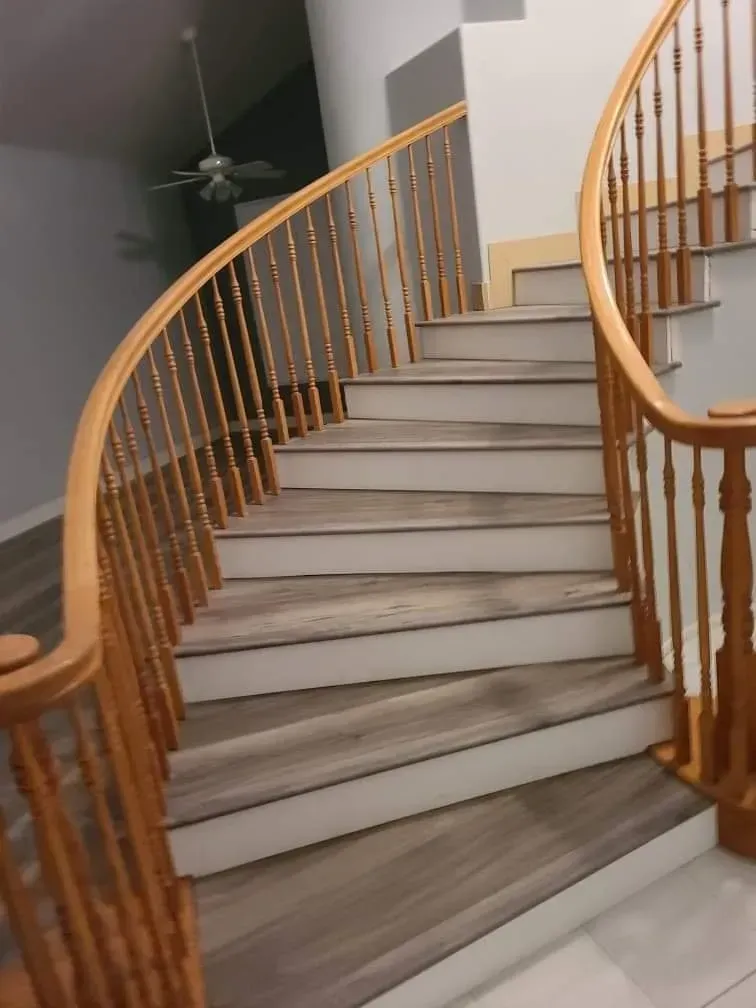 A curving staircase with light wood-look treads, white risers, and a wooden handrail with vertical balusters.
