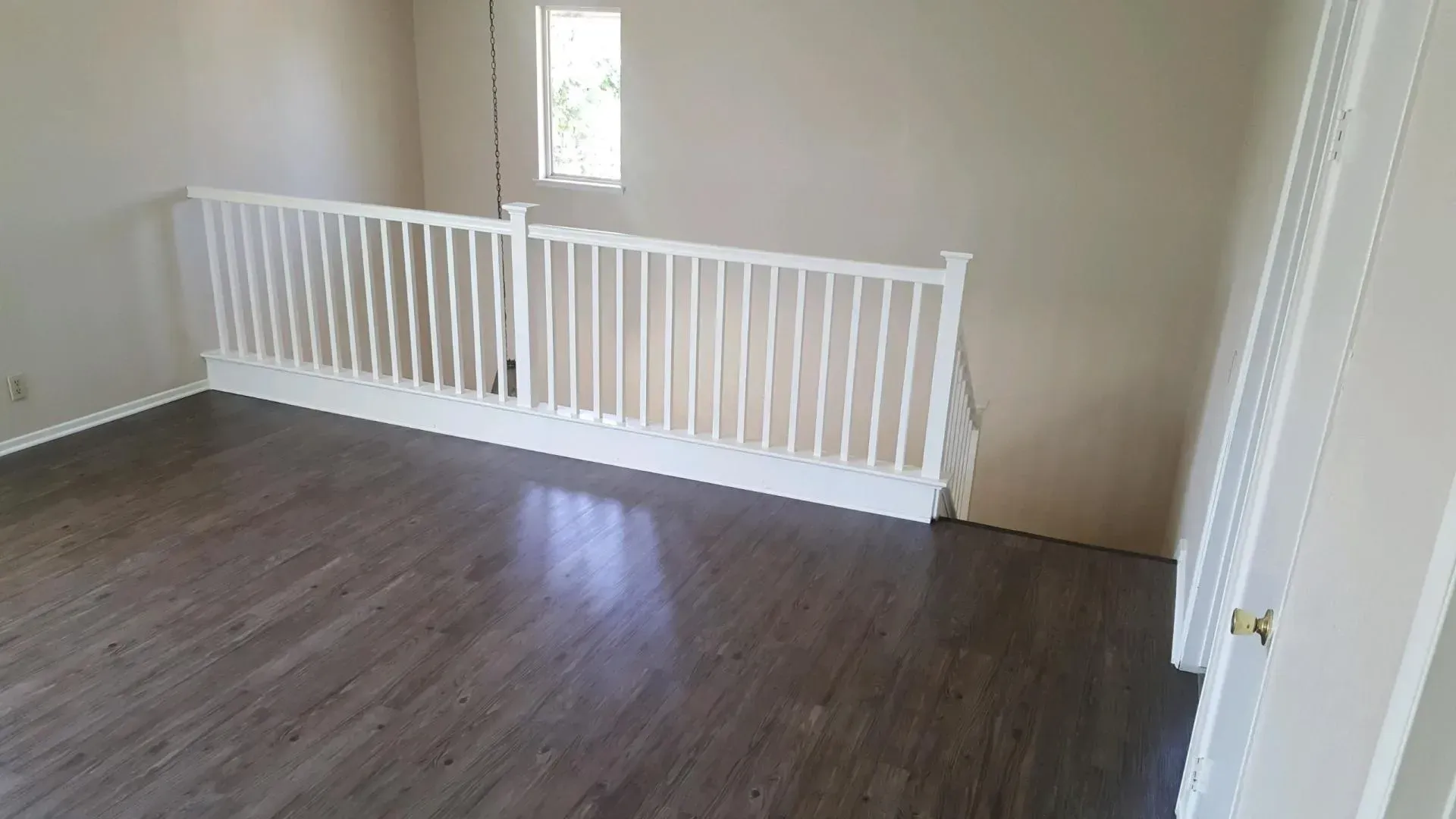 A view of a carpeted landing featuring dark wood-look floors, a white railing overlooking stairs, and a single window.
