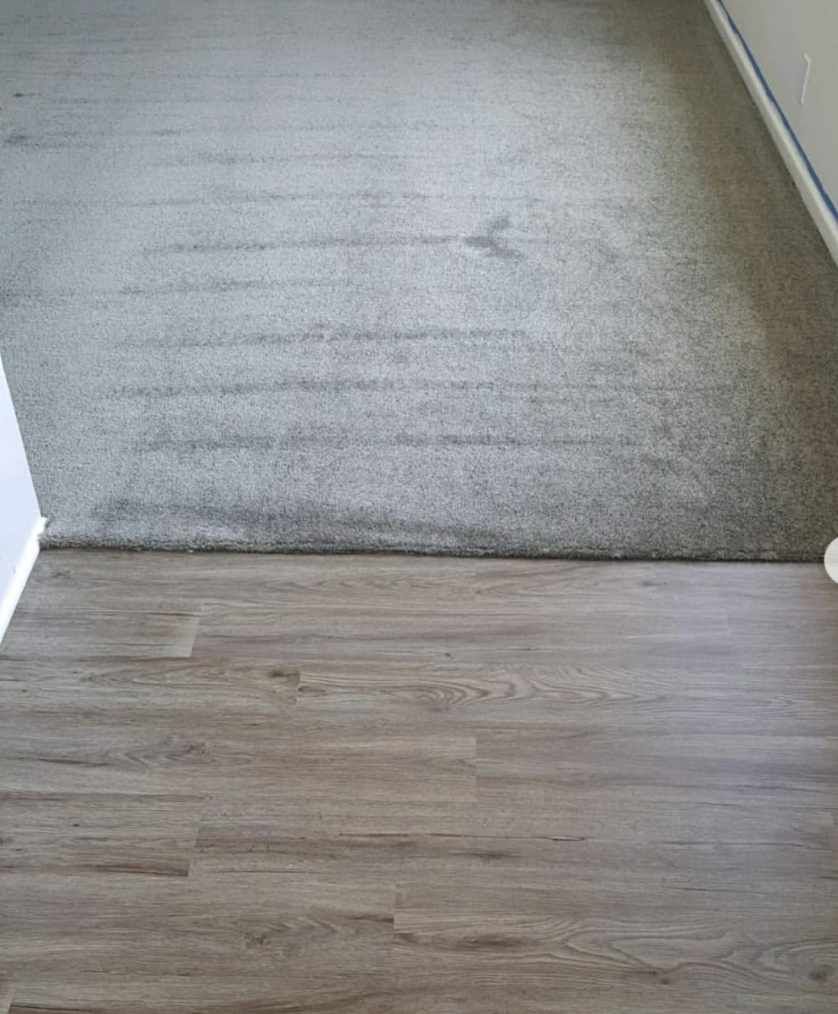 A split-floor view showing gray carpeting meeting gray wood-look laminate flooring.