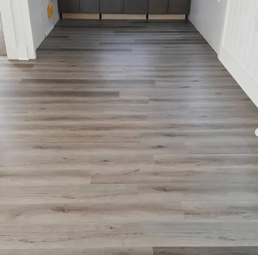 Light grey wood-look plank flooring installed in a residential room with white trim and dark cabinets in the background.