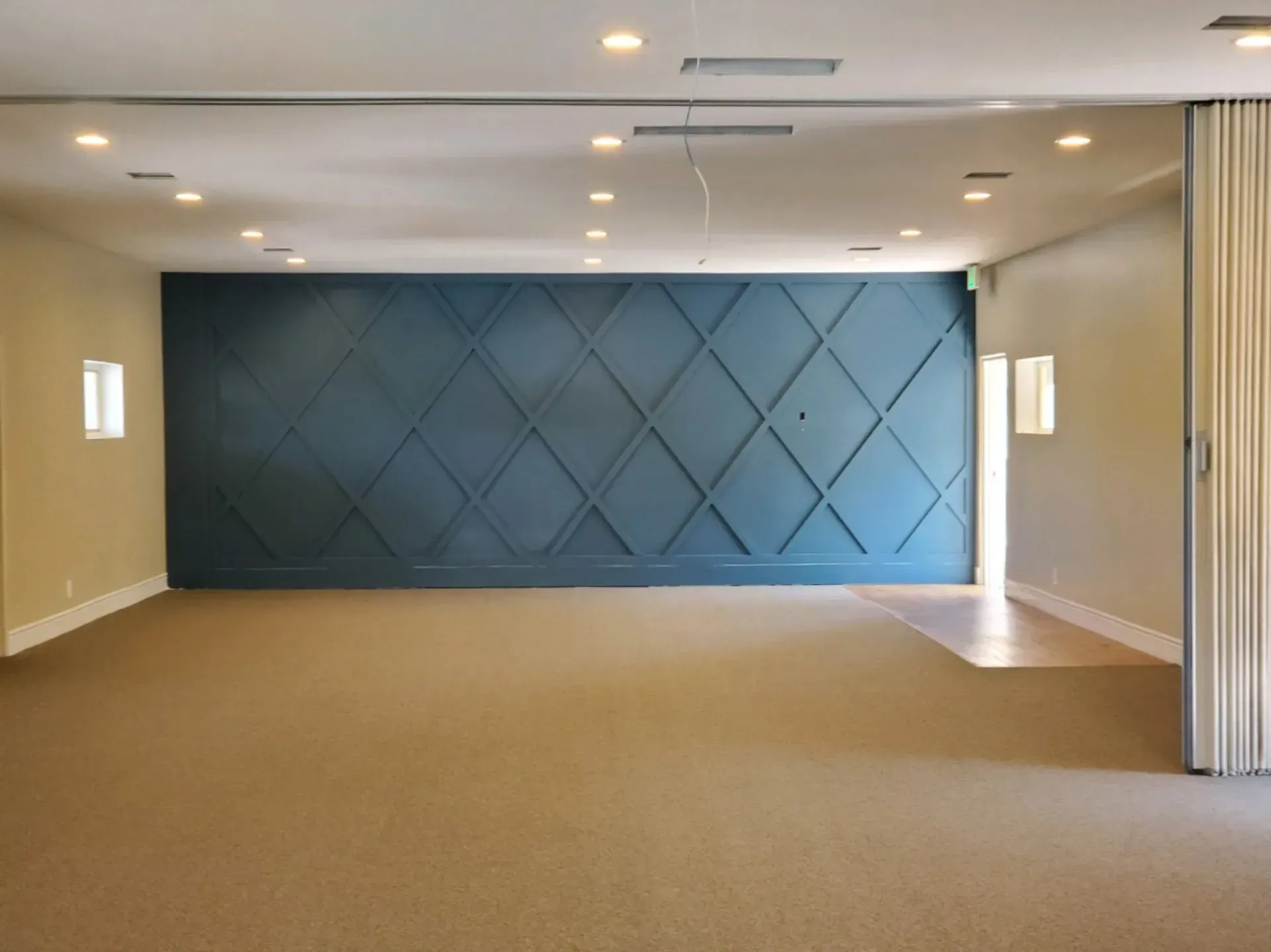 A wide, empty room features a large, dark blue accent wall with a geometric, diamond-pattern wood molding design.