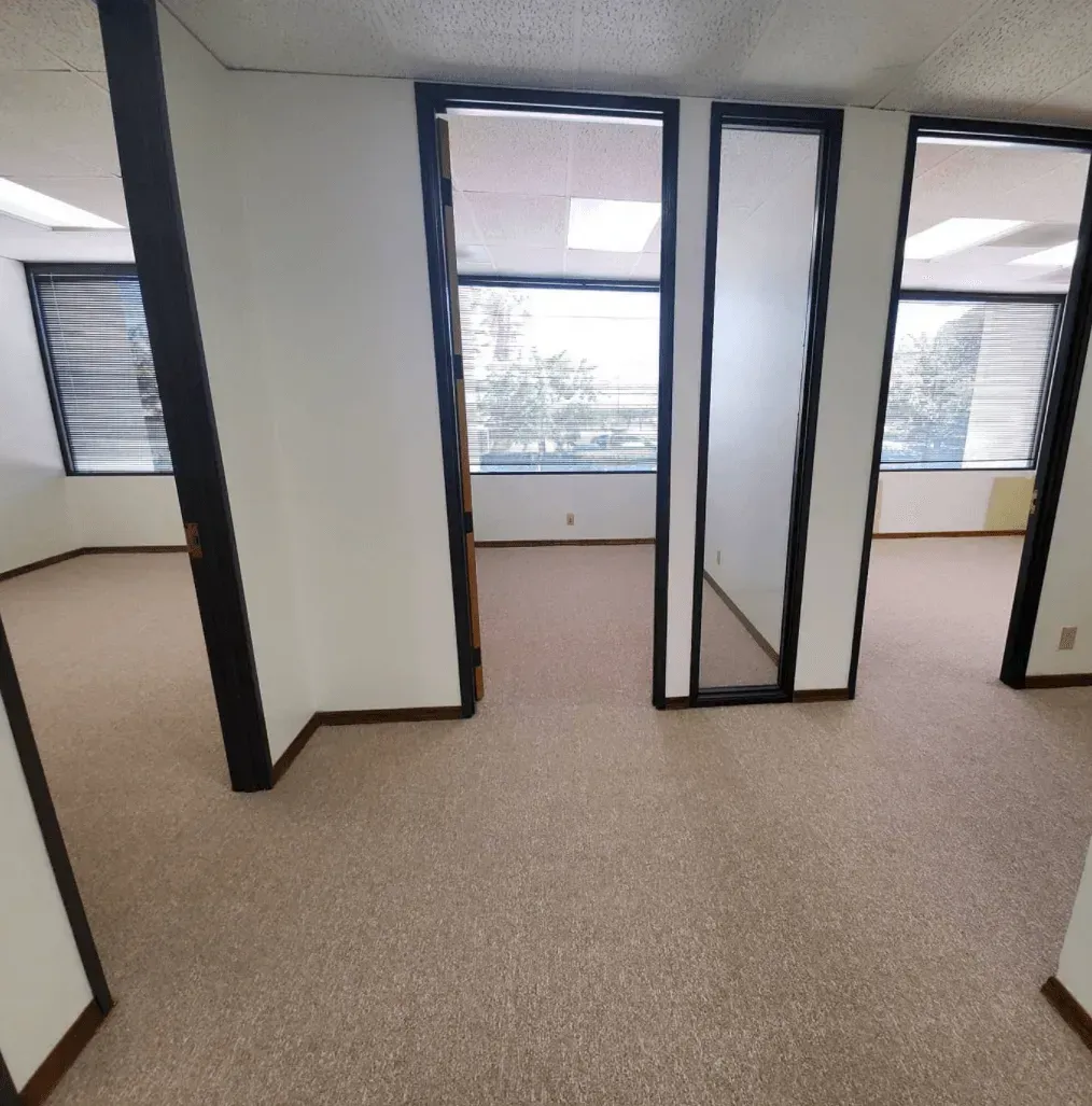 An office interior featuring beige carpet, white walls, and multiple doorways leading into small, empty workspaces.
