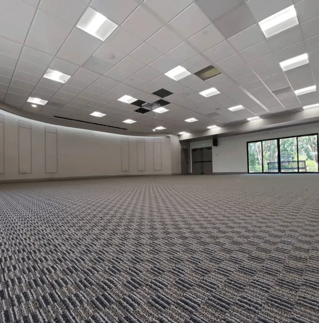 A wide, empty conference room with a patterned carpet, recessed ceiling lights, and floor-to-ceiling windows.