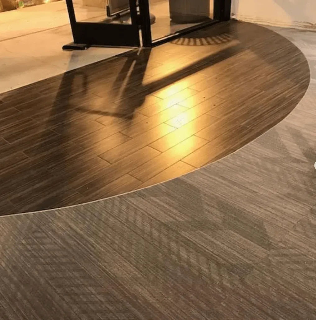 A transition from gray carpet to a semi-circular area of dark wood-look floor tiles near a glass doorway.