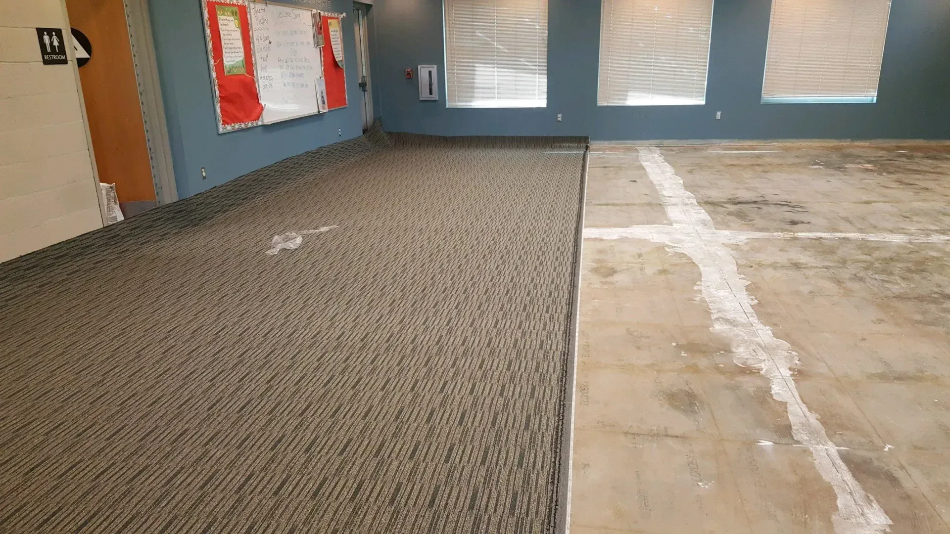 An interior room showing a transition from new carpet installation to an exposed concrete floor with white filler seams.