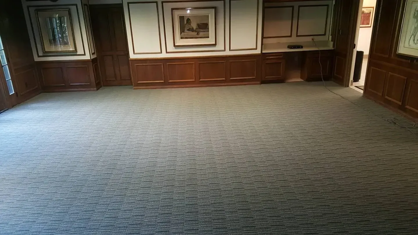 A room featuring paneled wooden walls, framed artwork, and a large, textured grey carpet covering the entire floor.