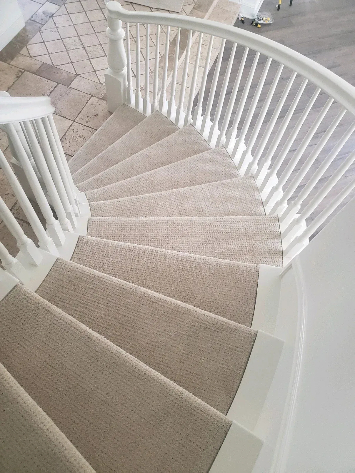 A curved staircase with beige carpet treads and white wooden railings, seen from a high-angle perspective.