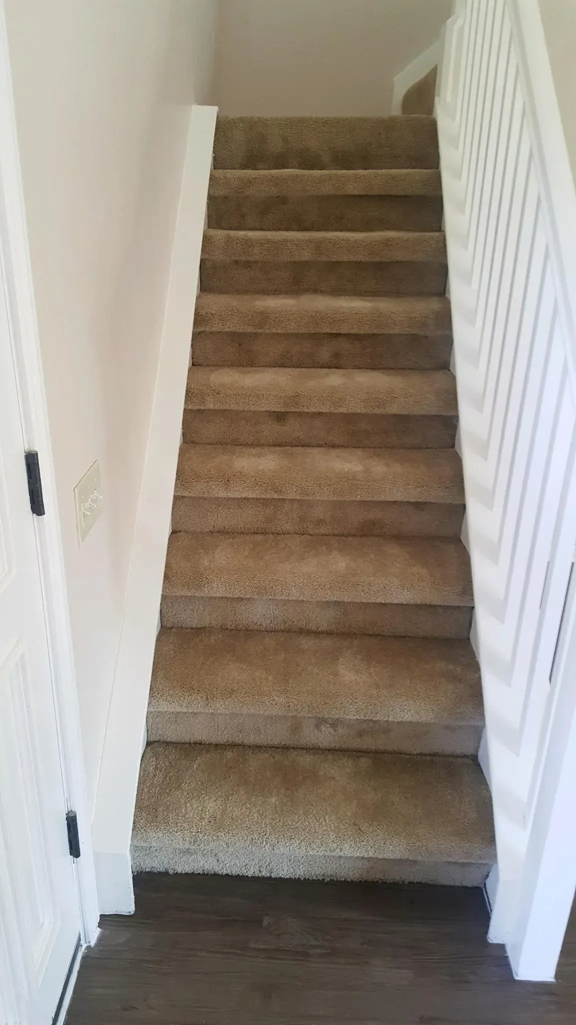 A set of carpeted stairs leading upward between two white walls in a home interior.