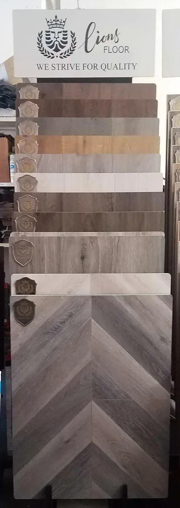 A vertical display of various wood flooring samples in shades ranging from dark brown to light gray and white.