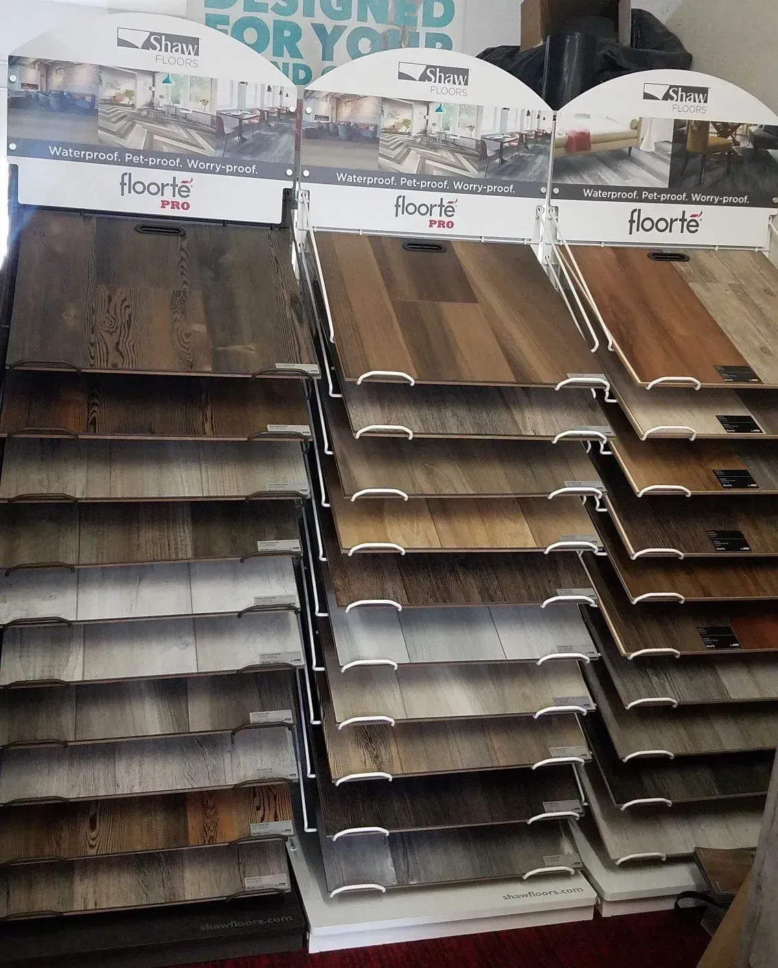 A retail display rack featuring various wood-look laminate or vinyl flooring samples in brown, gray, and tan tones.