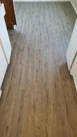 A narrow hallway with light-brown wood-look luxury vinyl plank flooring between two white doorways.