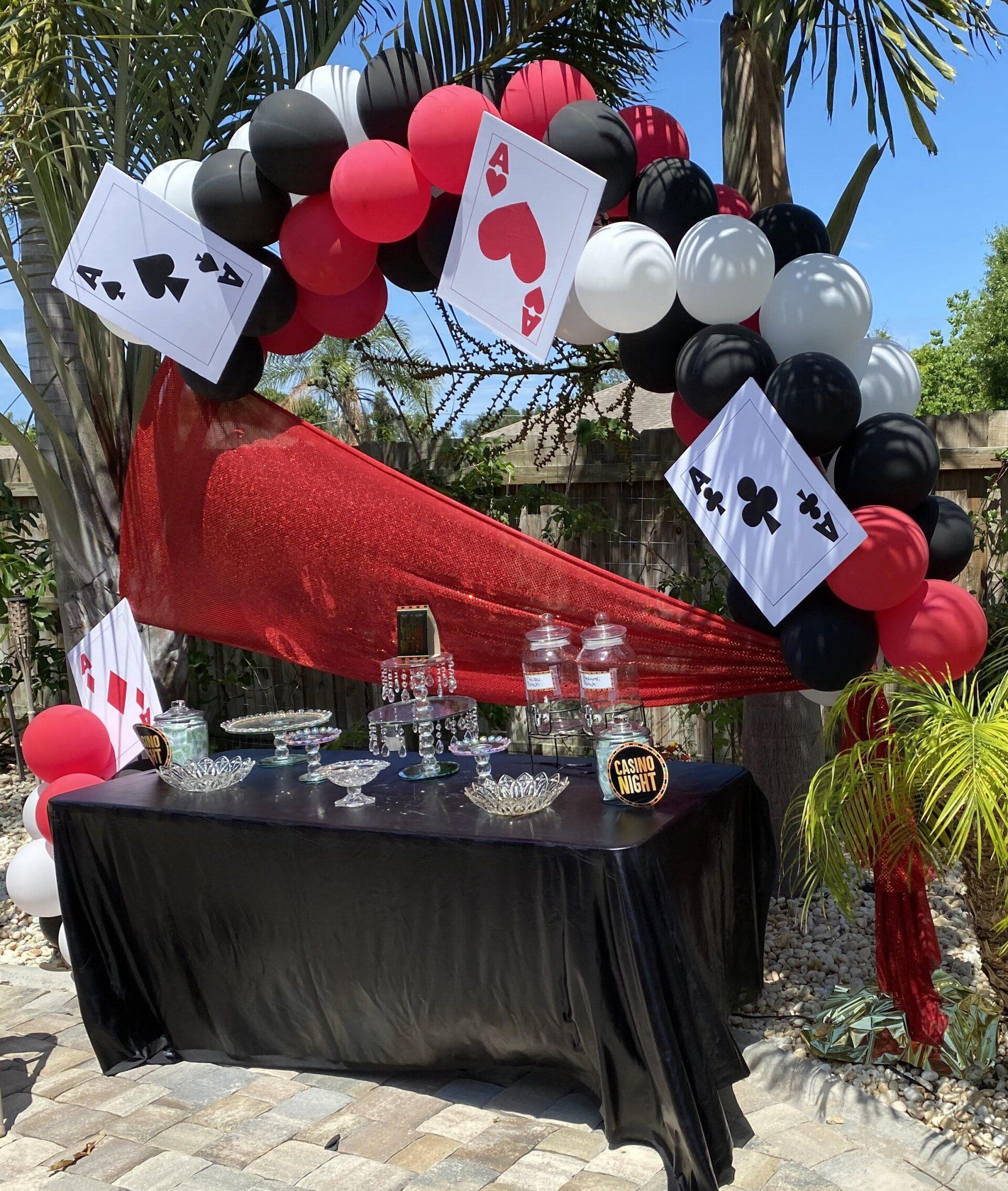 Red and black casino-themed balloon arch over a decorated table outdoors