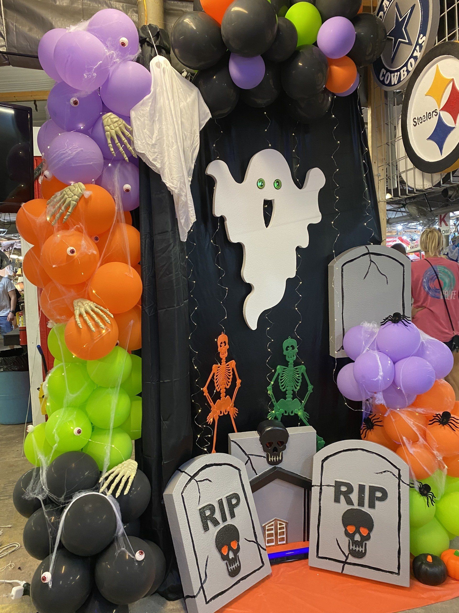 Halloween graveyard scene with purple, orange, green, and black balloon arch, ghosts, and RIP tombstones
