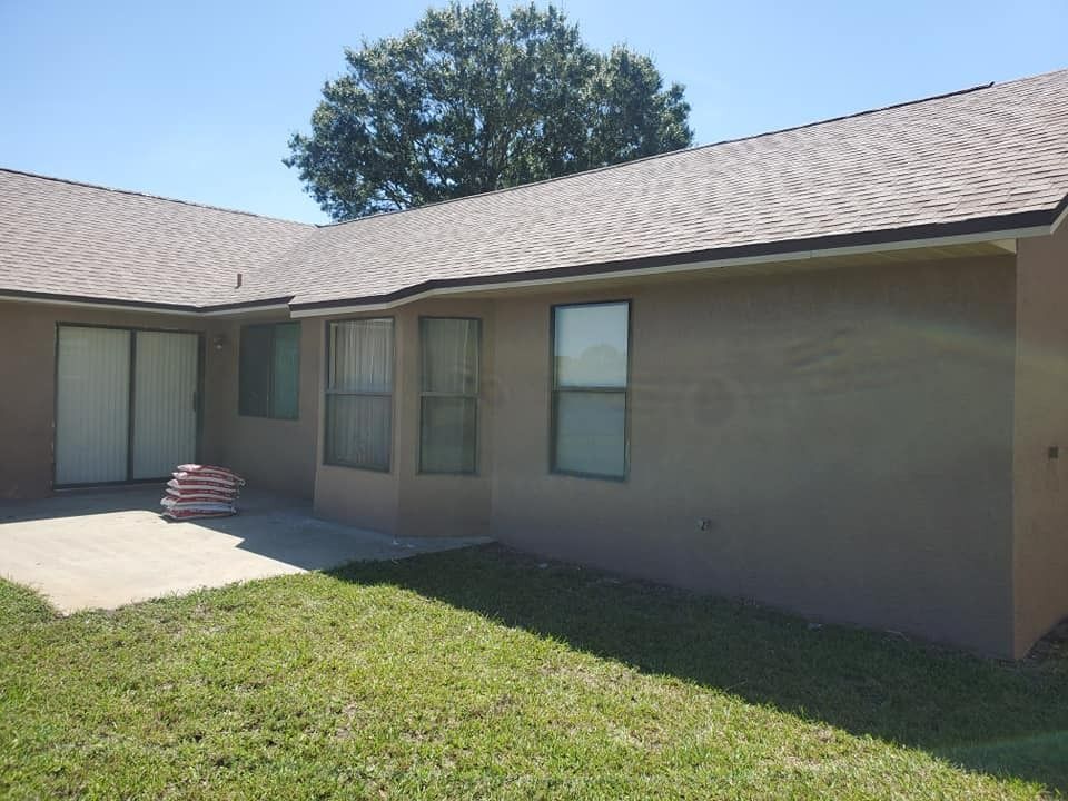 Single-story stucco house exterior with tan walls, small windows, and a green lawn in front