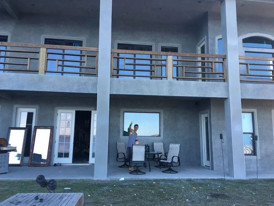 Two-story balcony house with patio furniture and large windows in front.