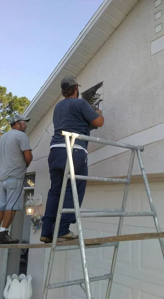 Two workers on a ladder painting a house exterior near the roofline