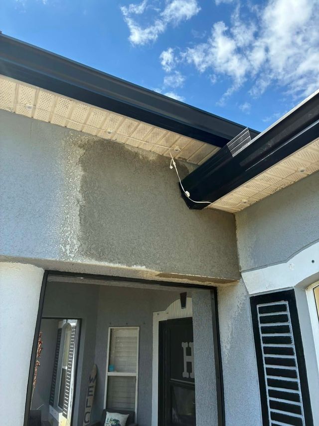Covered front porch with gray stucco walls, black beams, and a blue sky above.