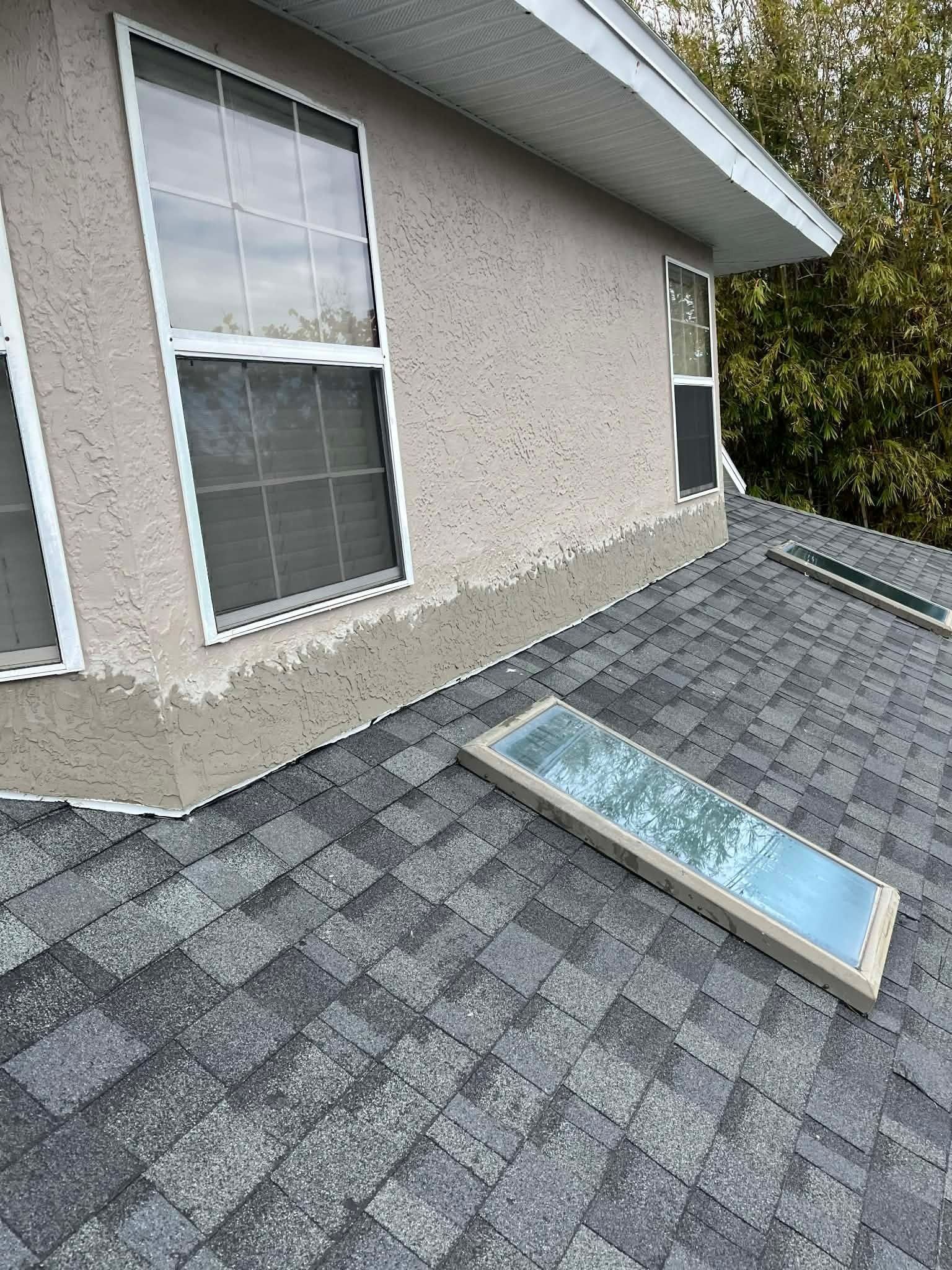 Roof shingles beside house wall with a skylight lying flat on the roof.