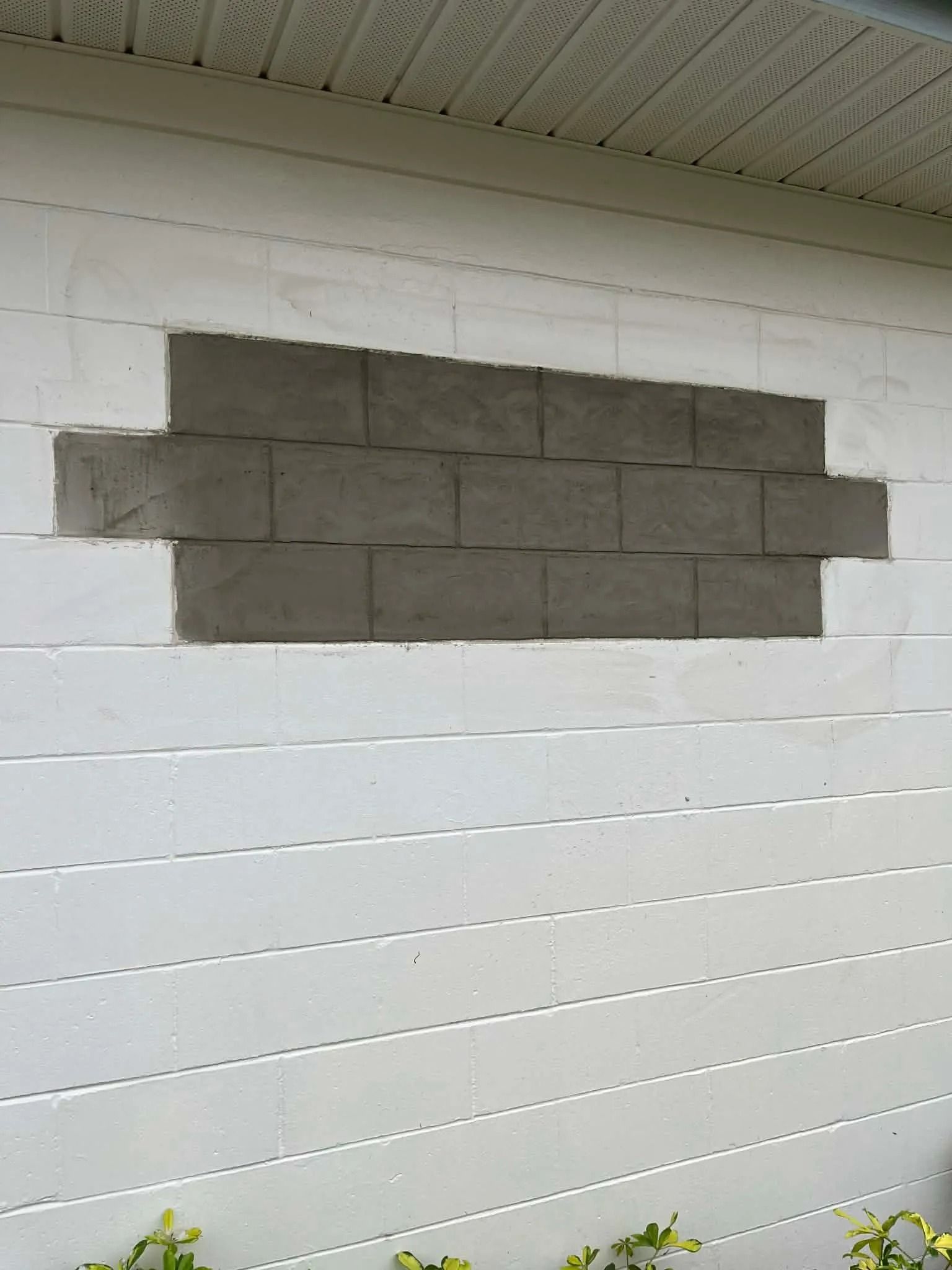Gray cinder blocks patching a hole in a white exterior wall near the roofline