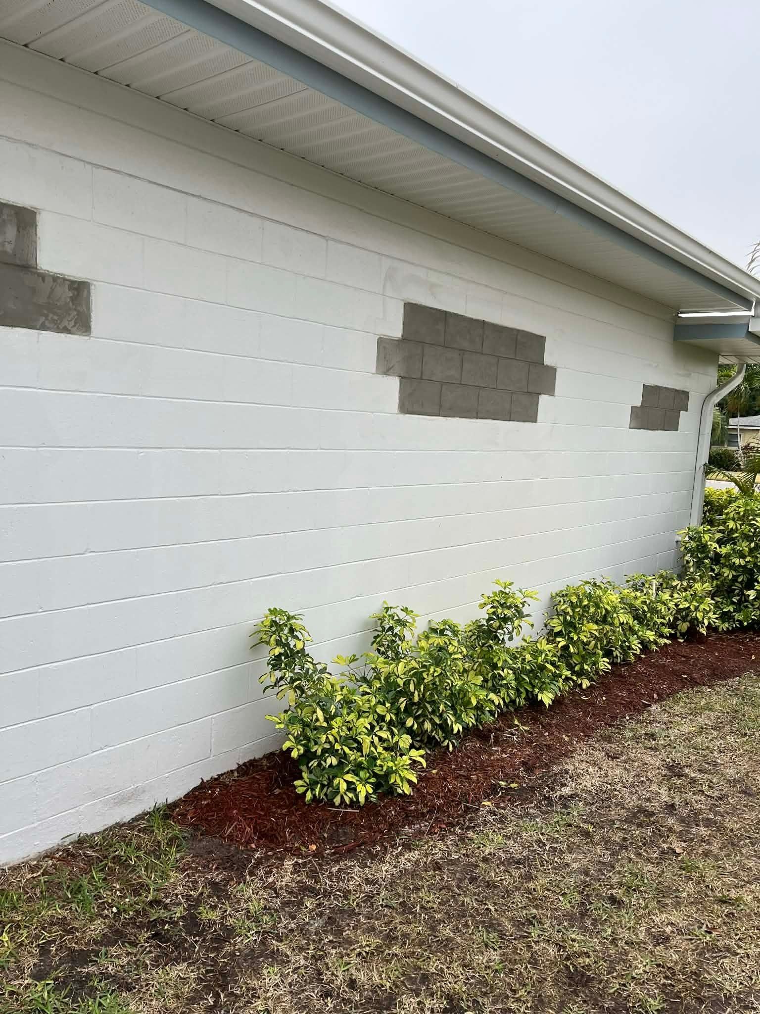 White exterior wall with small shrubs and a red mulch bed under a house eave