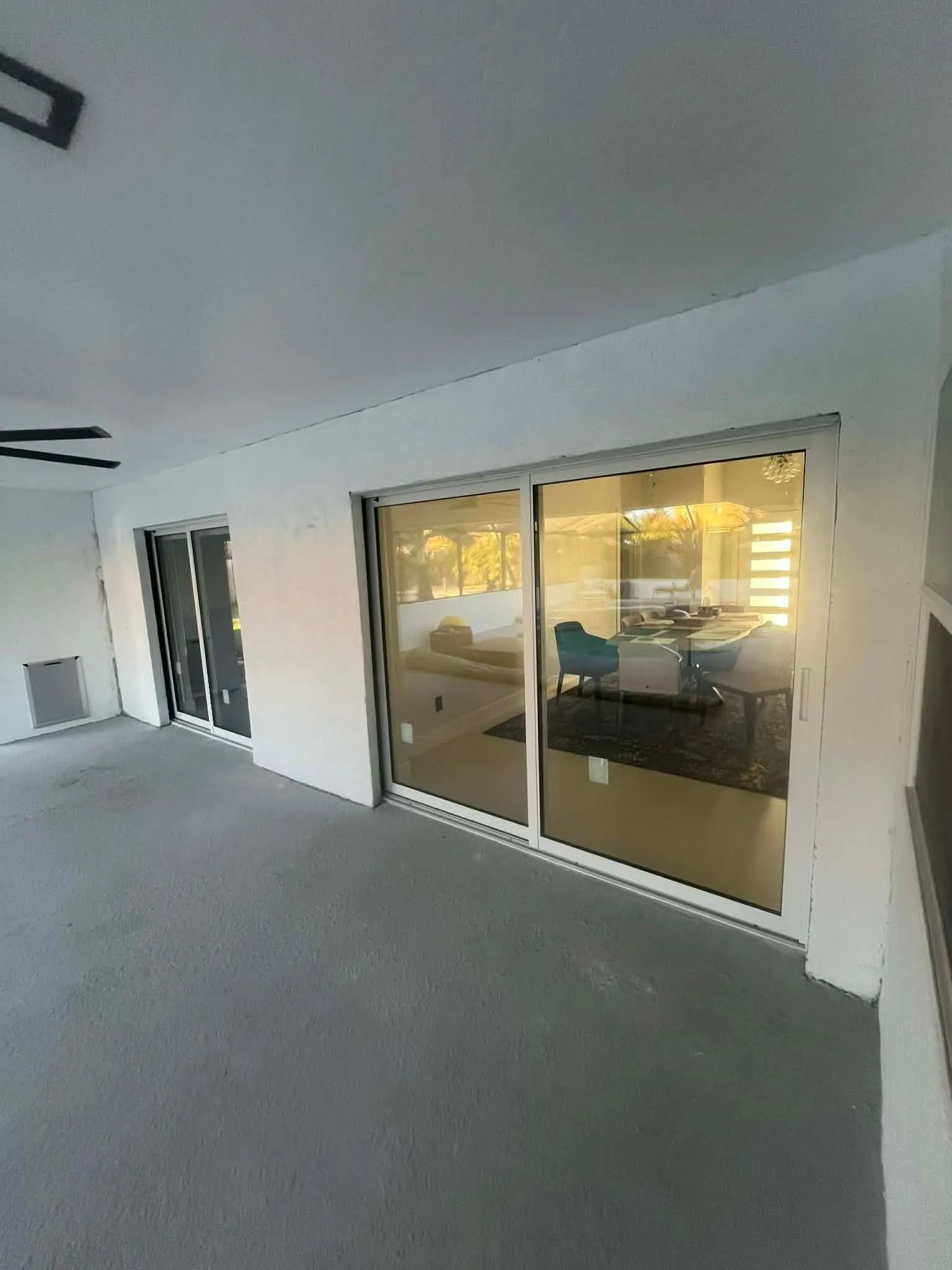 Empty covered patio with gray carpet, white walls, and sliding glass doors to a lit interior.